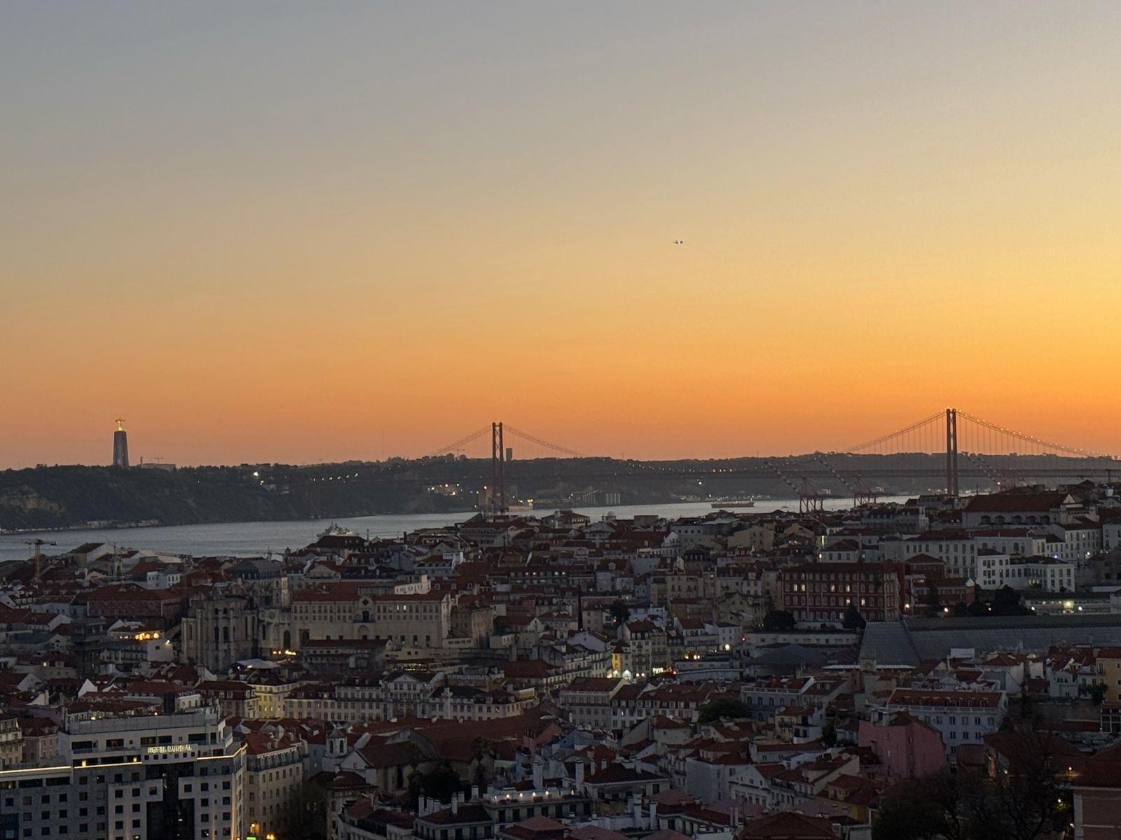 The 25 de Abril Bridge and the Cristo Rei statue glowing at dusk above Lisbon’s rooftops